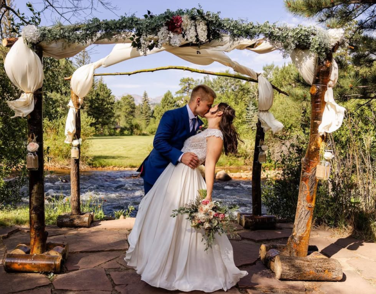 Estes Park Wedding Itinerary Inspiration, Couple posing at Romantic RiverSong Wedding Arch